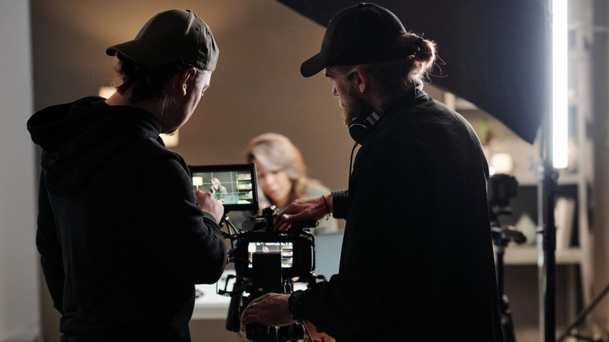Back view of two young men standing in front of camer aand using steadicam while shooting new commercial with female model